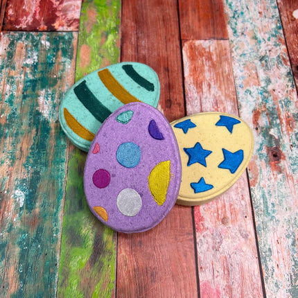 three easter egg bath bombs (purple, green & yellow) on a multi-color background